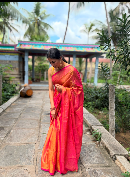 woman wearing pink linen tissue saree standing in the temple. the saree is shining under the sun 
