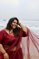 Woman in Blood Red Organza Saree with sheer flowing pallu at the beach — nylon organza with light shimmer, Label Anaira