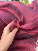 Hand holding Blood Red Organza Saree fabric with blurred outdoor background — Label Anaira