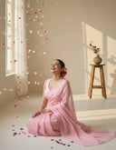 Model seated wearing Blushy Blush light pink organza saree with flowing pallu and soft floral accents