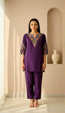 Woman wearing a purple embroidered outfit in a well-lit room.