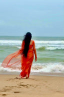 Back view of The Marigold Mischief orange and gold organza saree by Label Anaira flowing in the ocean breeze.