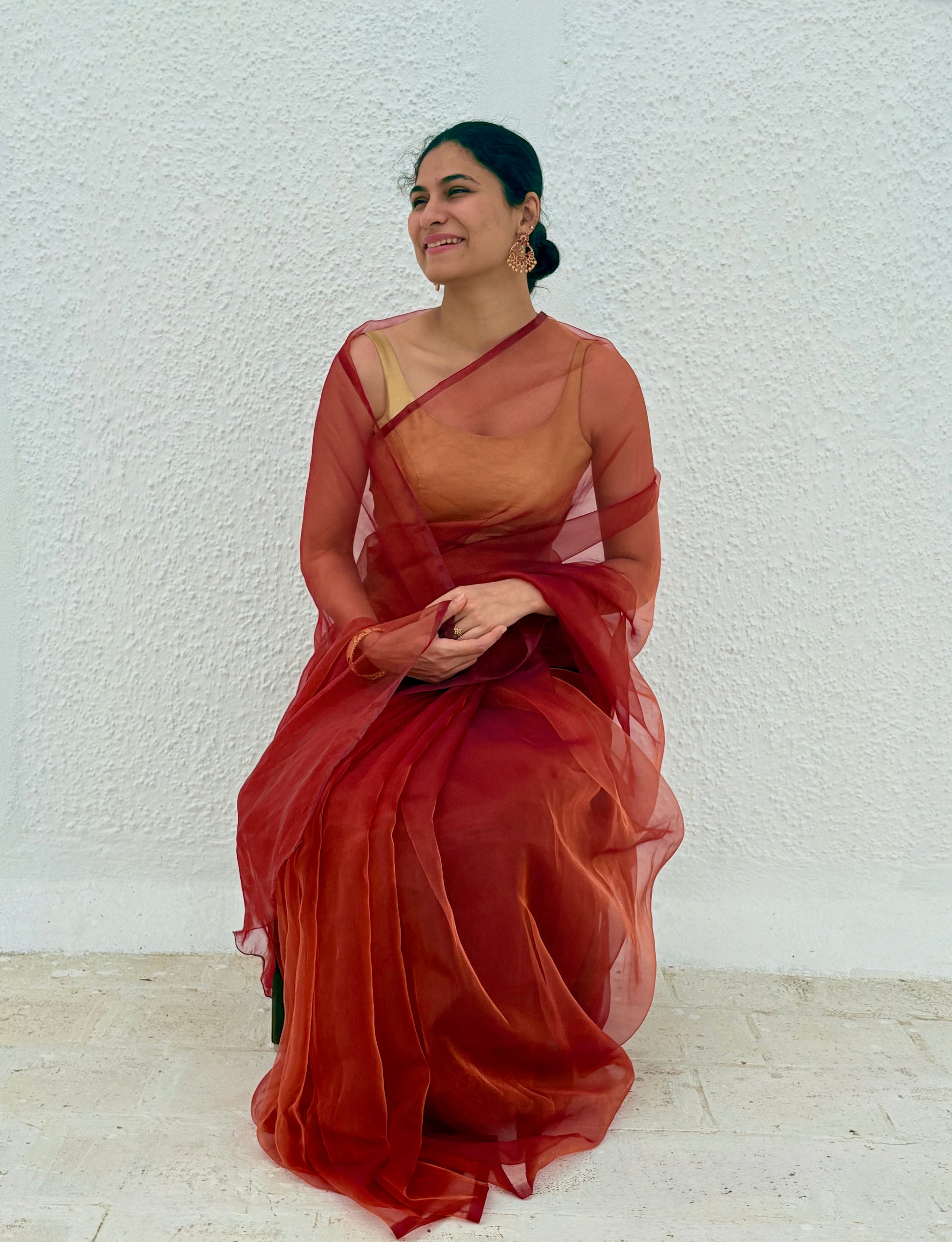 person  wearing red maroon orange pink and gold shade organza saree 