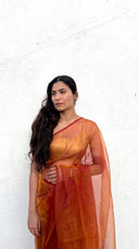 Front view of The Sunset Debutante saffron organza saree by Label Anaira, a lightweight sheer saffron saree glowing with warm amber tones.